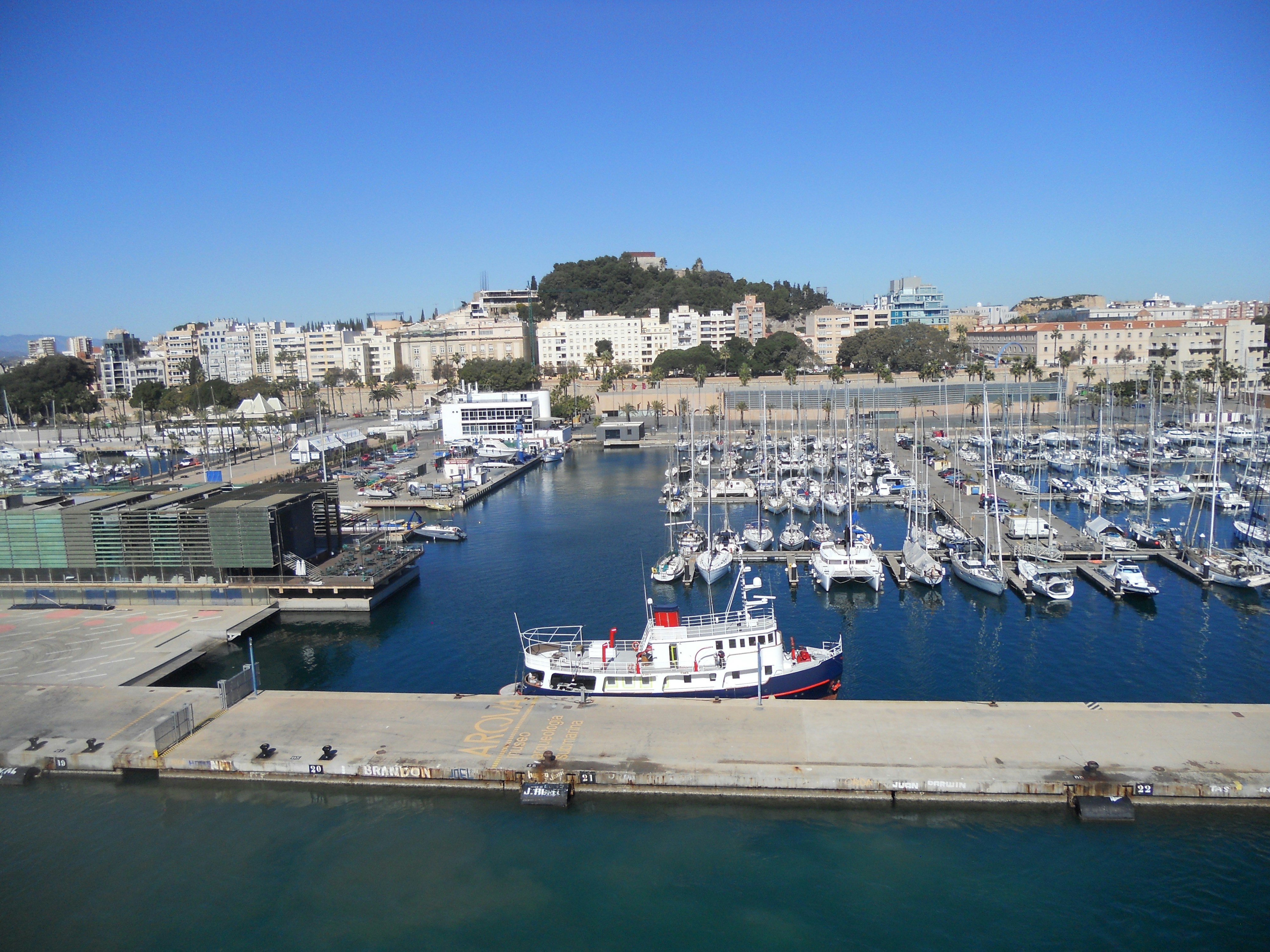 Boats in Cartagena harbour with the city and hillside beyond, showing the maritime side of this popular day trip from Murcia.